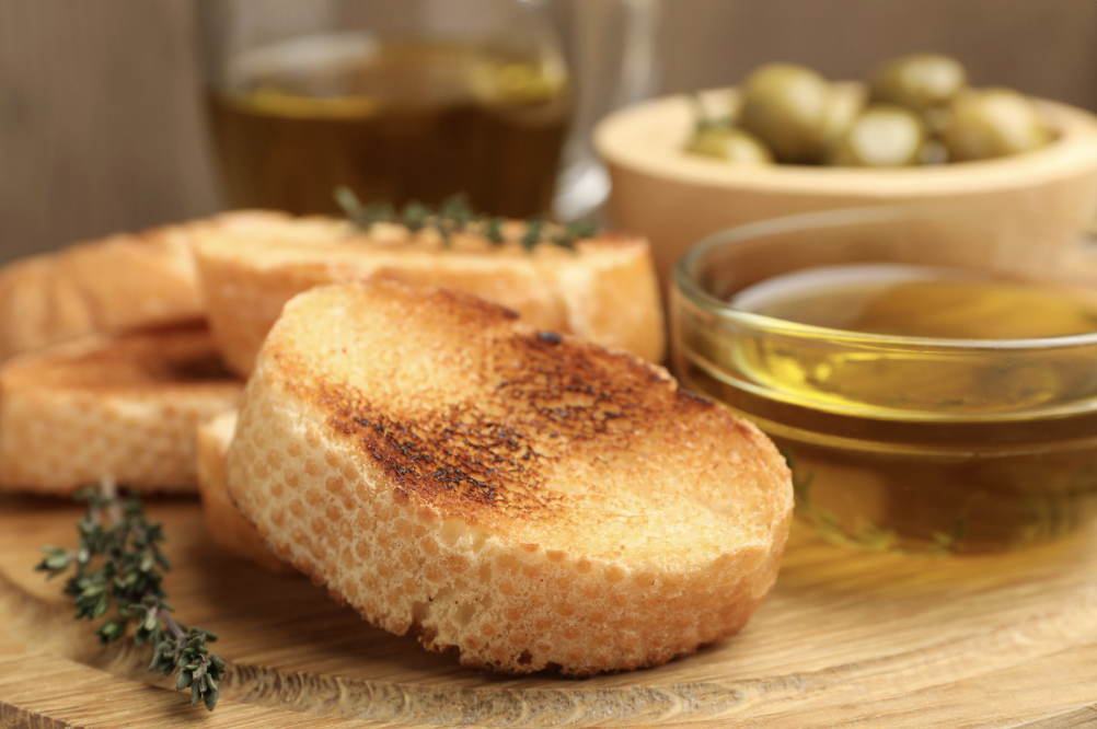 fresh cut garlic bread with olive oil and olives on wooden cutting board