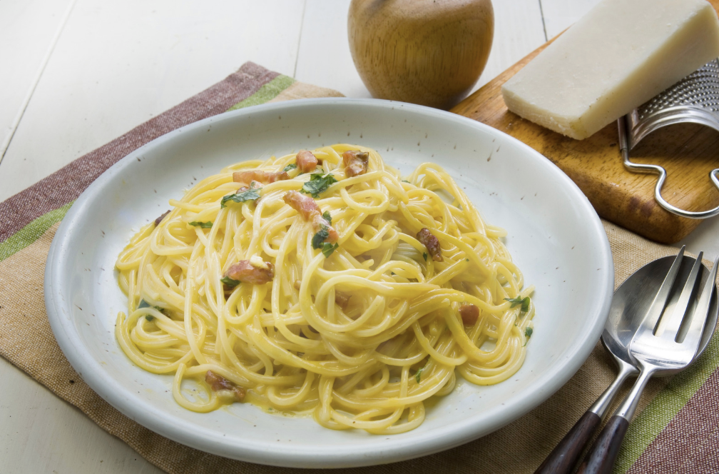 carbonara pasta in white dish on multi-colored placemat
