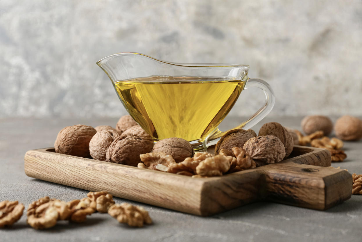 small pitcher of walnut oil surrounded with walnuts on gray table