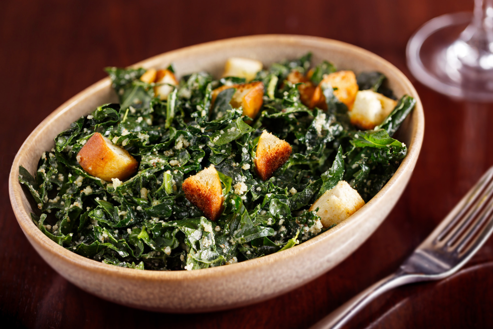 kale salad with croutons in wooden bowl on table
