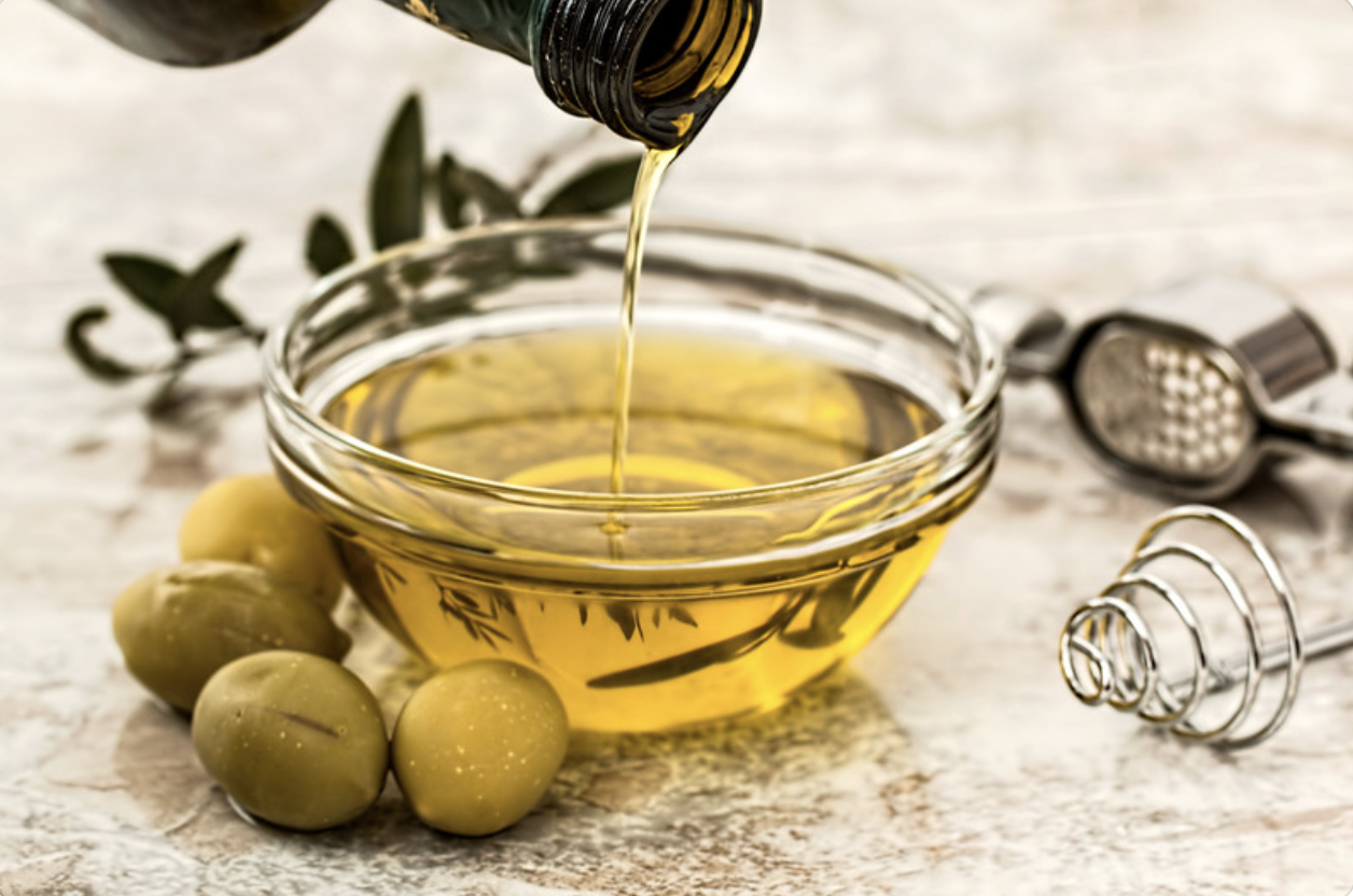 olive oil being poured into a bowl with whole green olives next to it