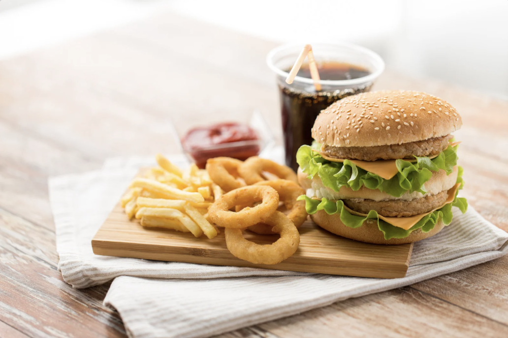 double cheeseburger, onion rings, french fries and soda on wood plank