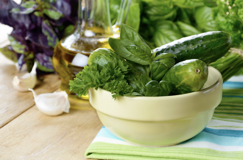 fresh herbs, cucumbers and garlic in bowl on wooden table