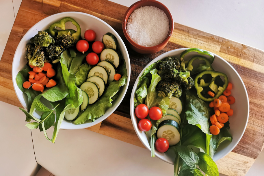 two bowls of fresh salad ingredients on wooden cutting board