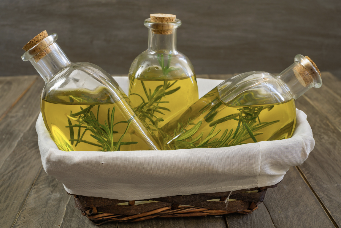 bottles of olive oil with rosemary in wooden basket with linen