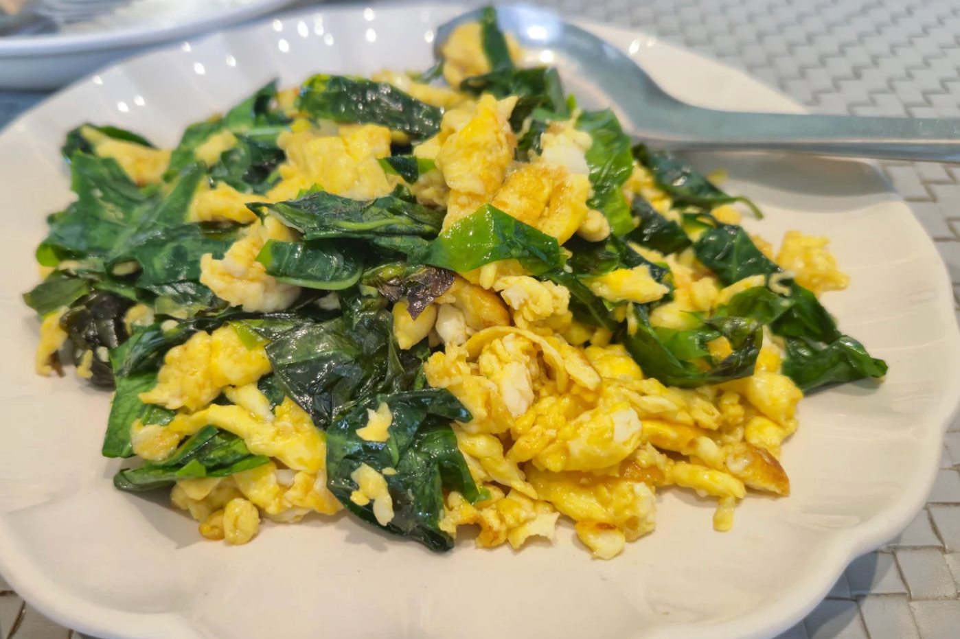 softly scrambled eggs with dark greens on white plate