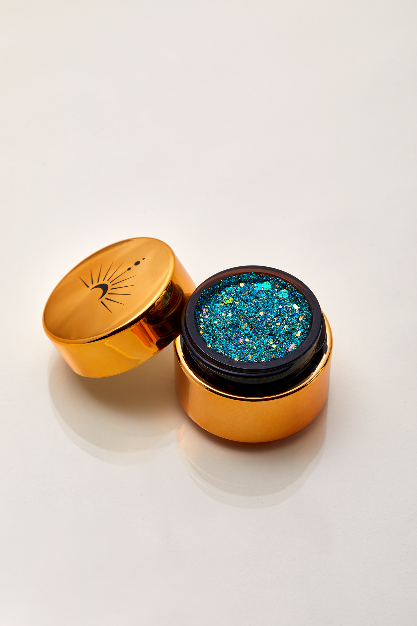 Sparkling array of blue teal turquoise green with flecks of gold and silver for a shimmering dramatic plant based glitter cream in a vegan non toxic formula dries to a water resistant  powder finish