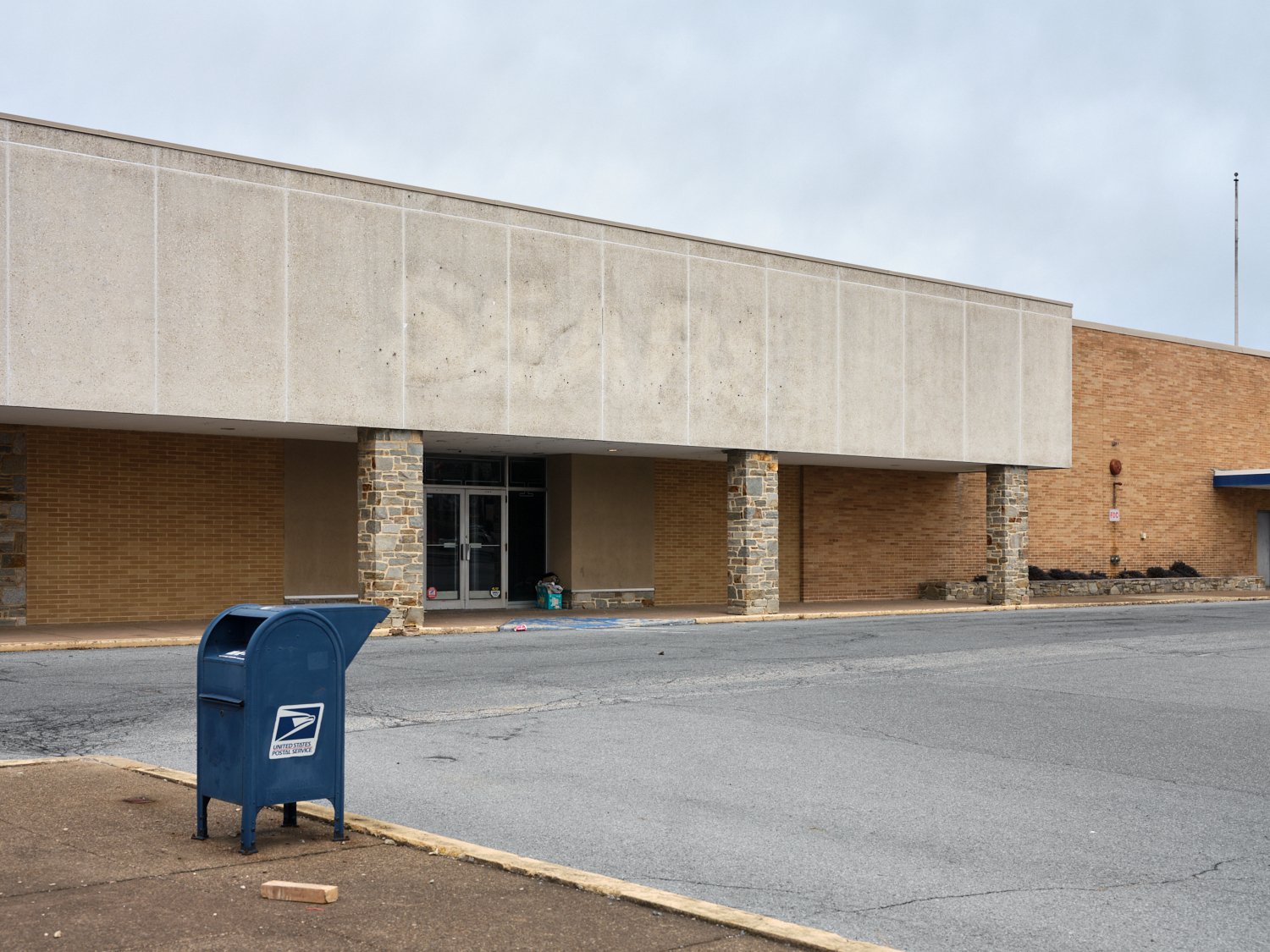 Empty parking lot in front of a brick and concrete building with a blue USPS mailbox in the foreground.