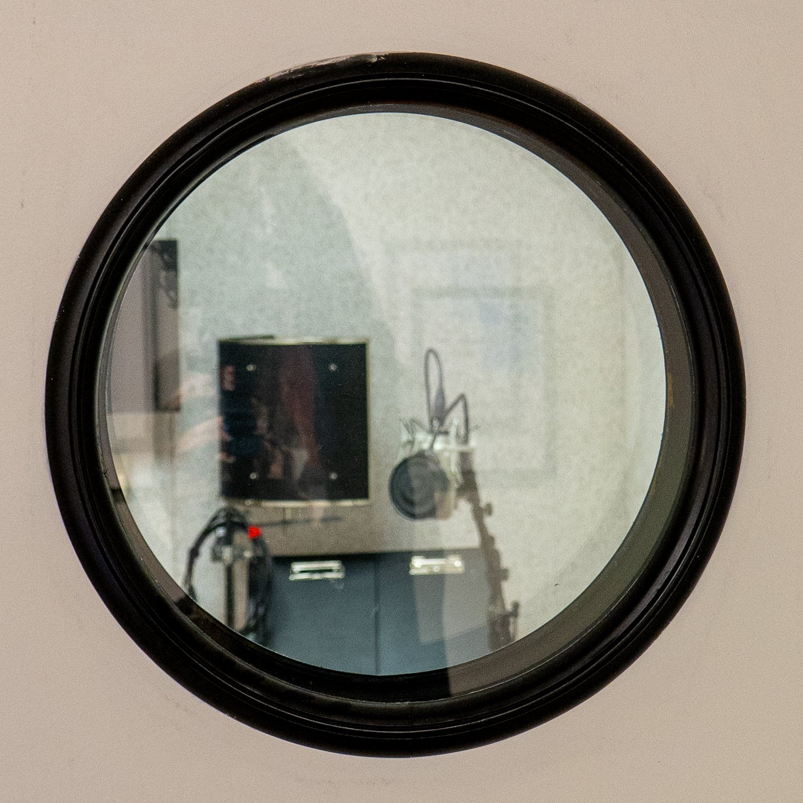 A washing machine viewed through its round glass door, showing a reflection of a room with a microphone, speaker, and audio equipment.