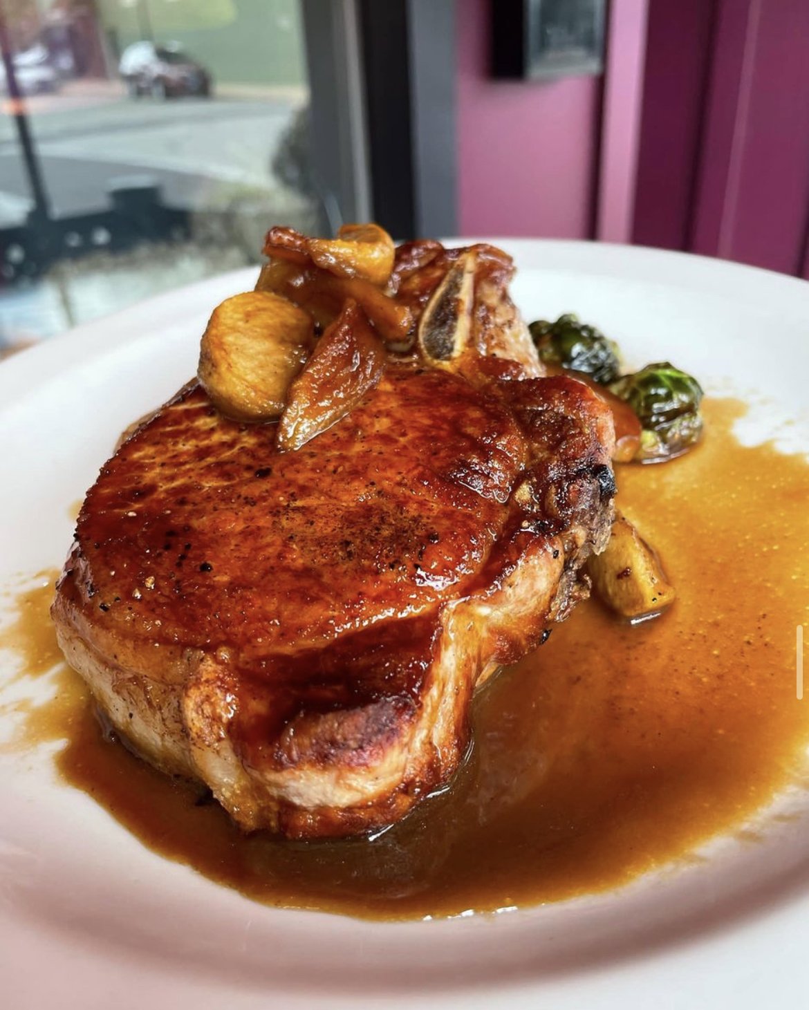 Juicy pork chop with mushrooms and sauce on a white plate, garnished with Brussels sprouts.