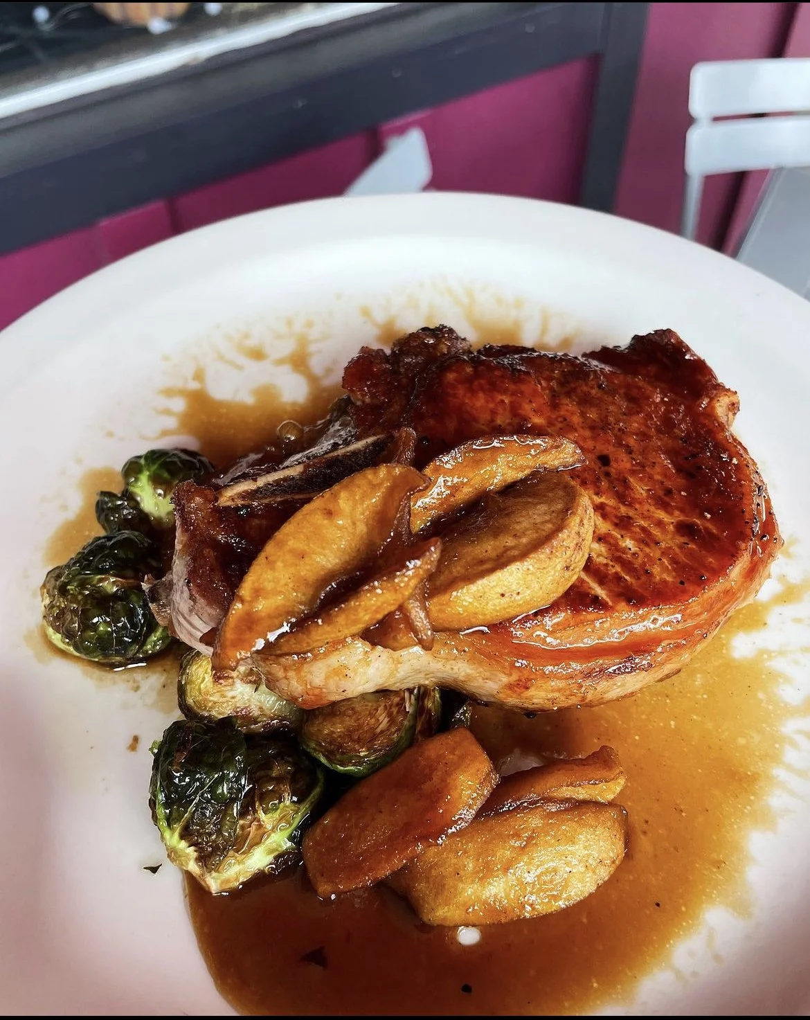 Grilled pork chop with apple slices, Brussels sprouts, and sauce on a white plate.
