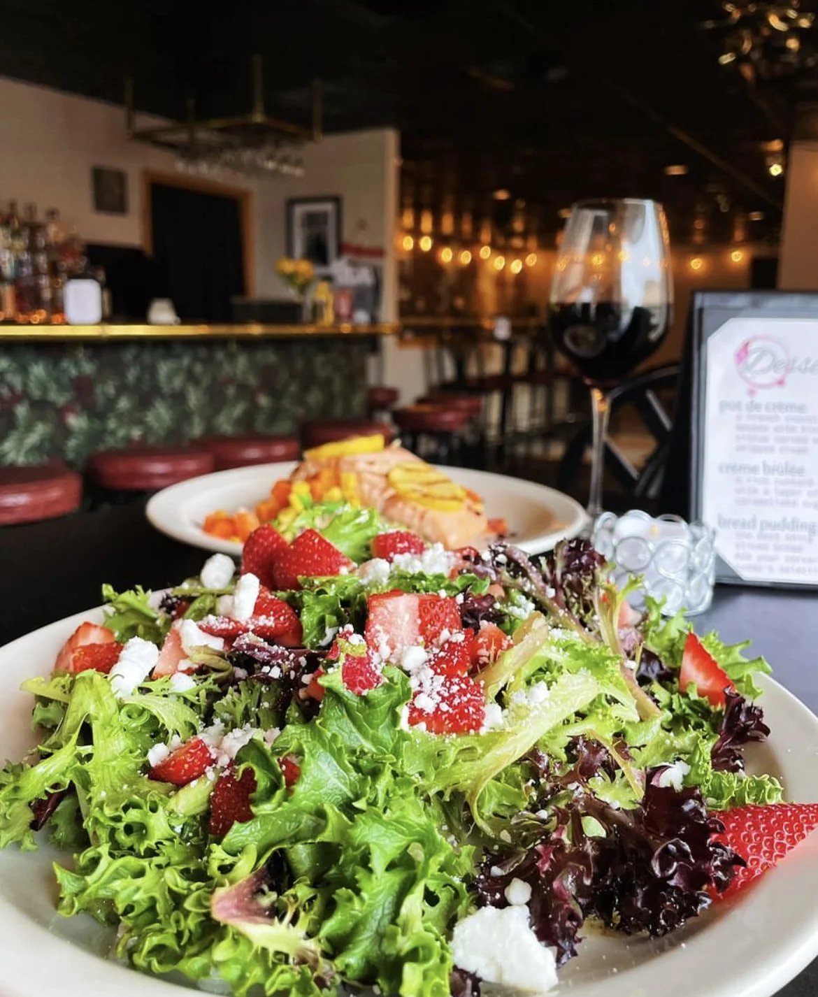 Fresh salad with strawberries and feta cheese, glass of red wine on table in restaurant.