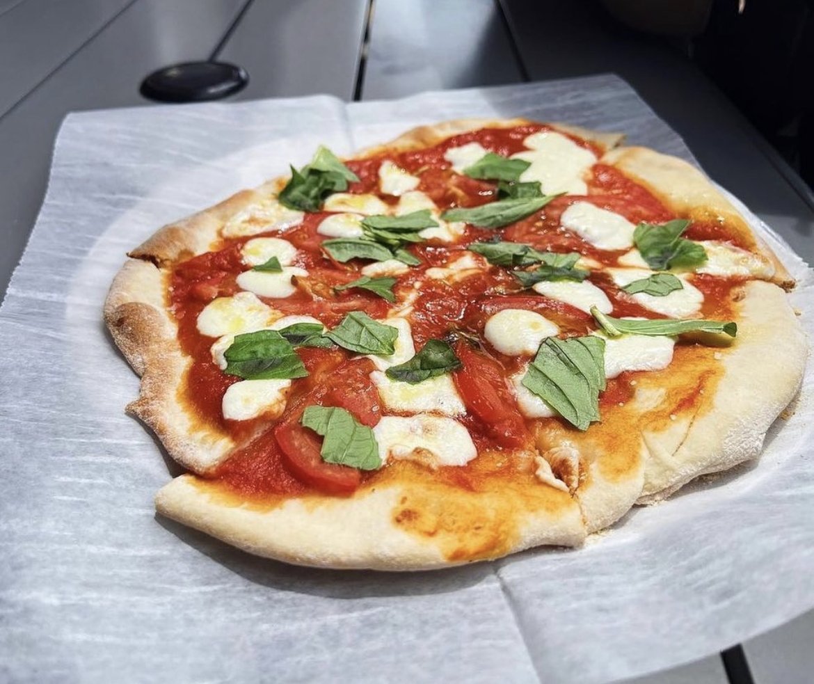 Thin crust Margherita pizza with tomato sauce, mozzarella cheese, and fresh basil leaves on parchment paper.