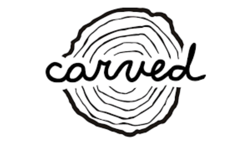 Close-up of a tree ring pattern with the Carved brand logo overlayed on it.