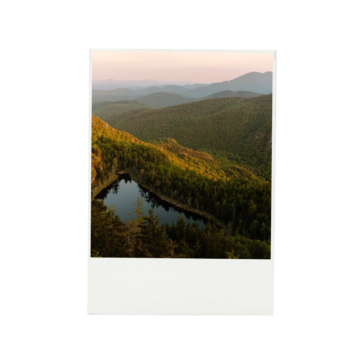 Aerial view of a mountain landscape with densely forested hills and a small lake reflecting the sky.