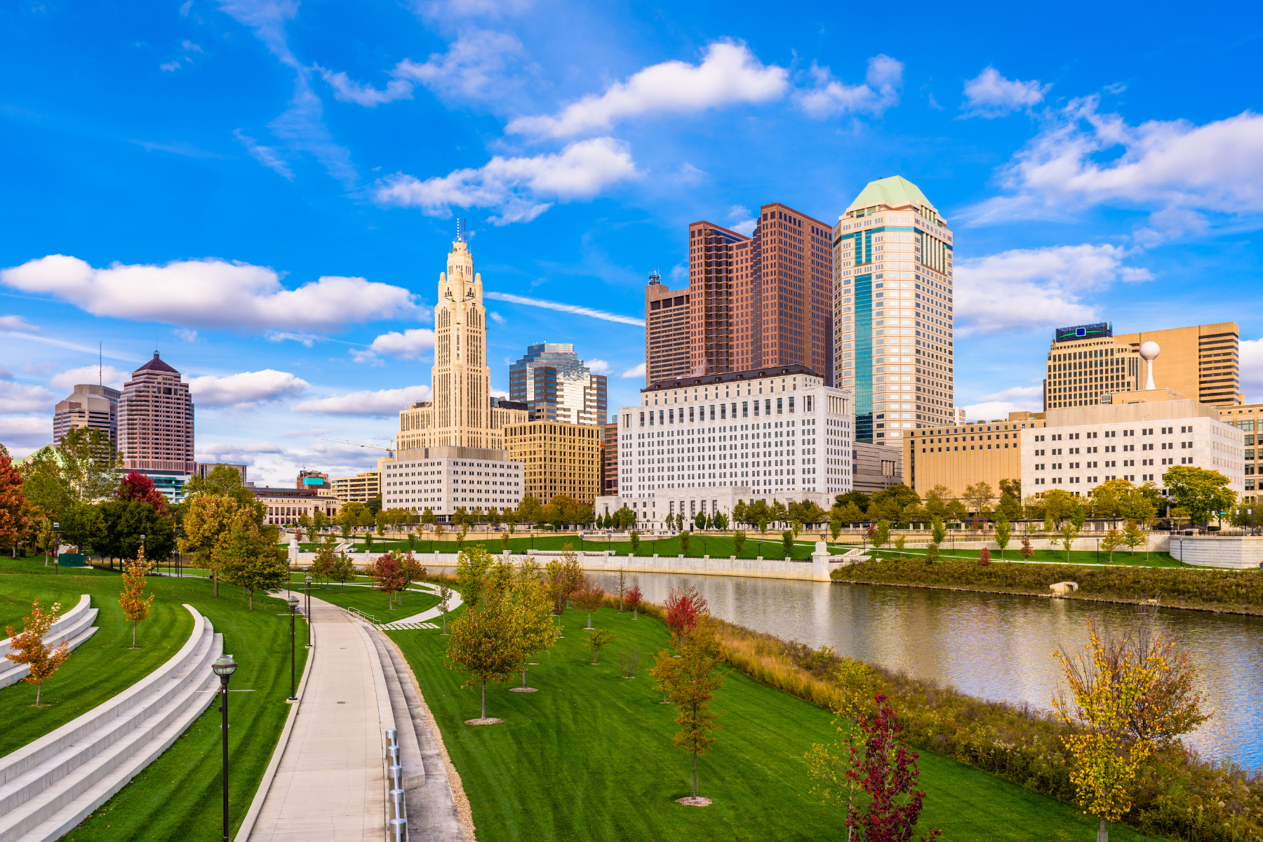 Columbus, Ohio skyline with skyscrapers, a river, and a park in the foreground on a sunny day.