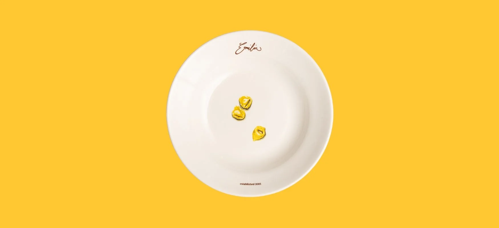 Three handmade tortellini on a white Emilia-branded plate set against a vibrant yellow background. A minimalist nod to Trattoria Emilia’s focus on traditional pasta and its reputation as one of the best Italian restaurants in Melbourne.