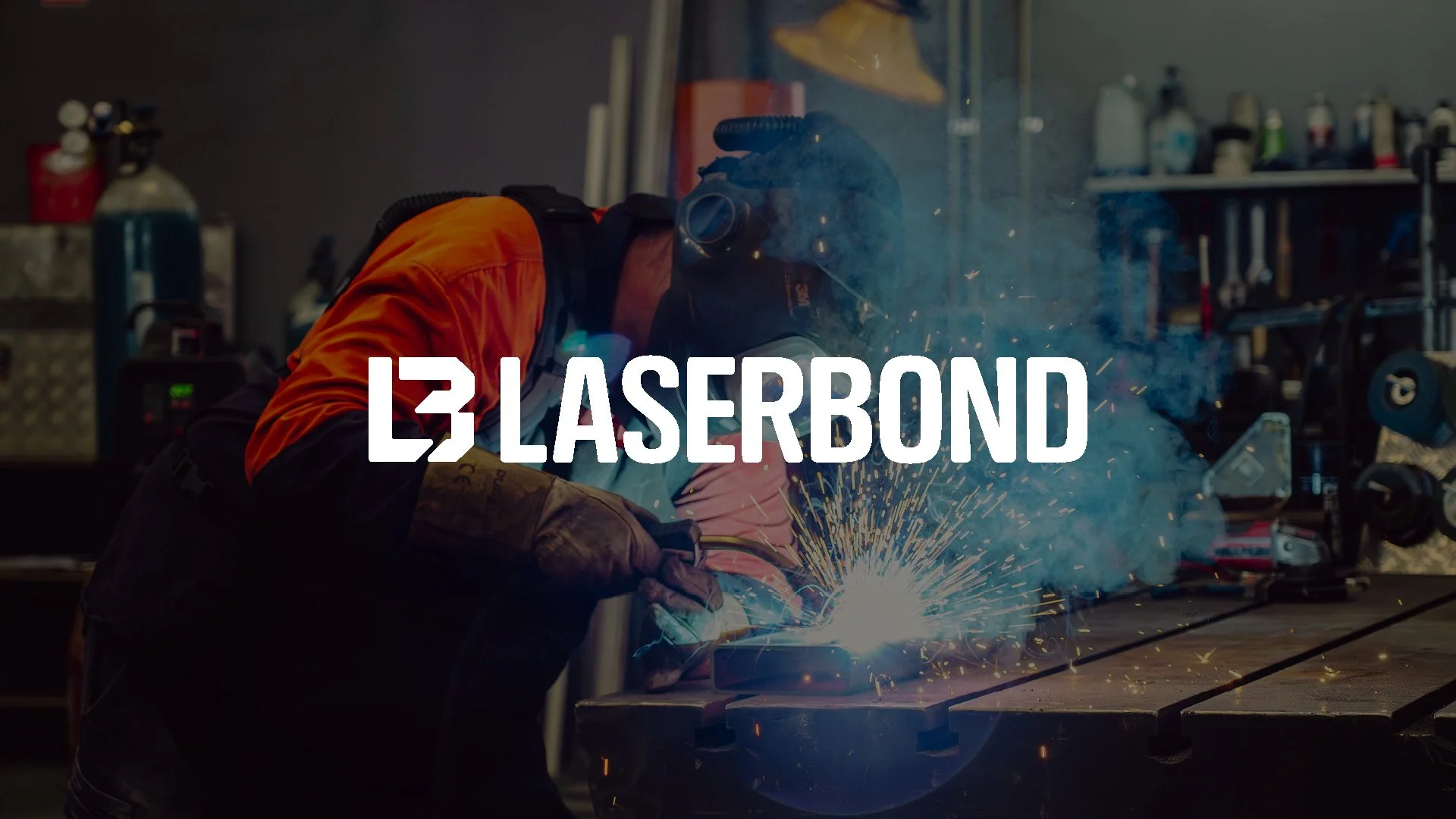 A man in safety gear welding at a workshop table with an orange hi-vis shirt.