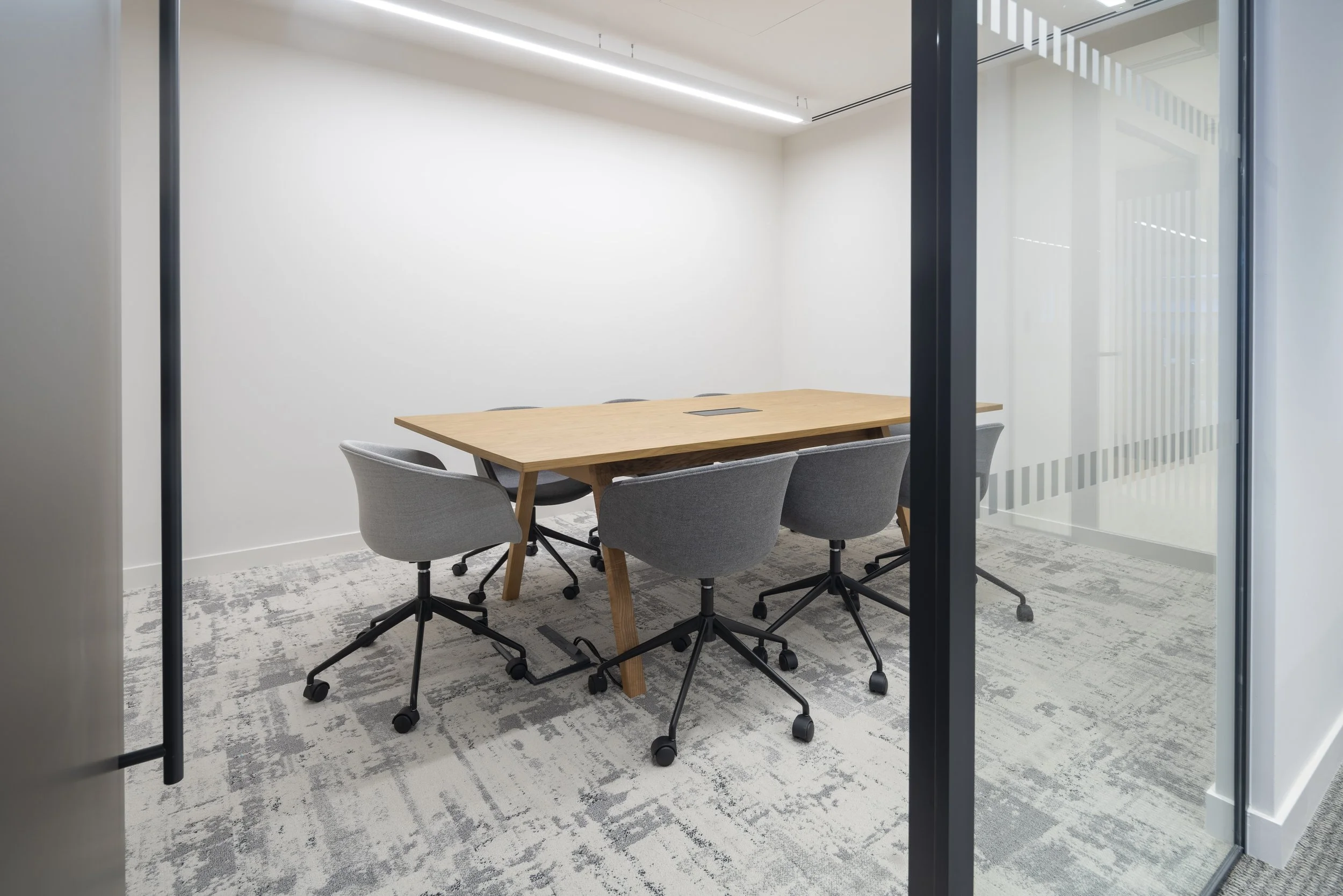 Empty modern conference room with a wooden table and six gray chairs, viewed through a glass wall.
