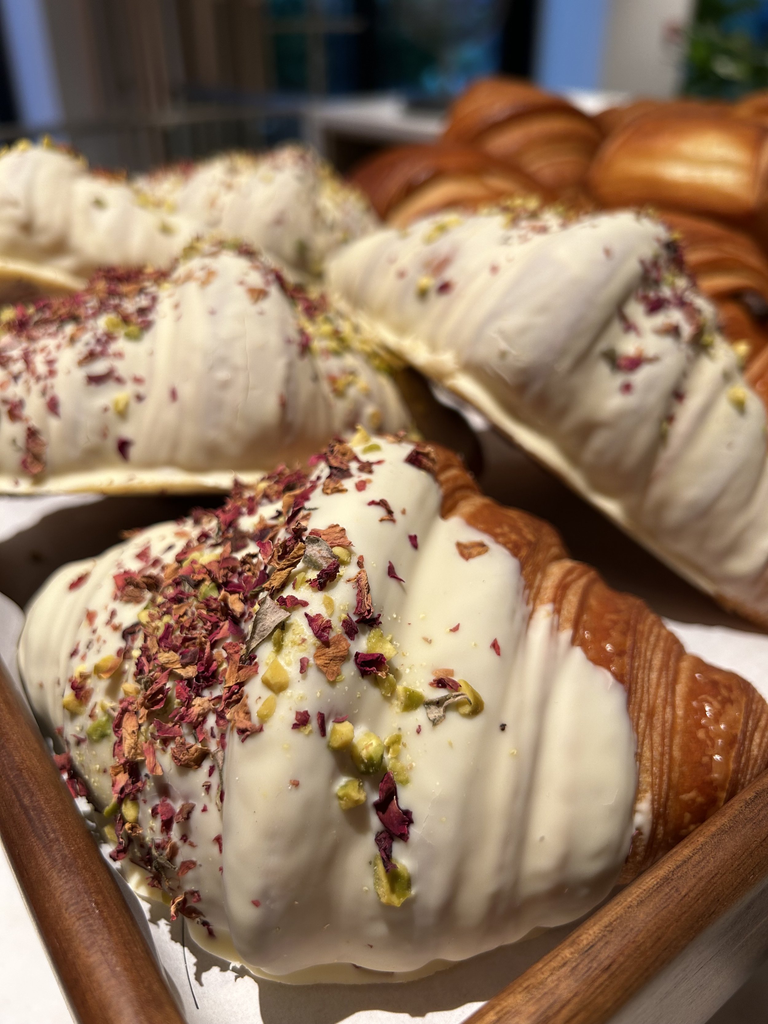 Close-up of a tray of croissants topped with white chocolate and sprinkled with dried rose petals and crushed pistachios.