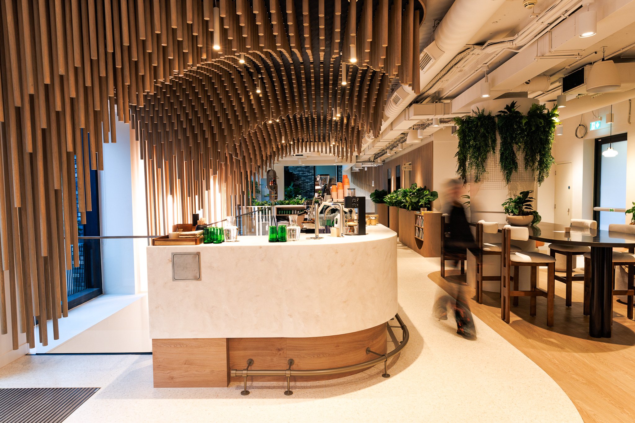 Modern cafe or restaurant interior with a marble counter, wooden decorative ceiling, and green plants.