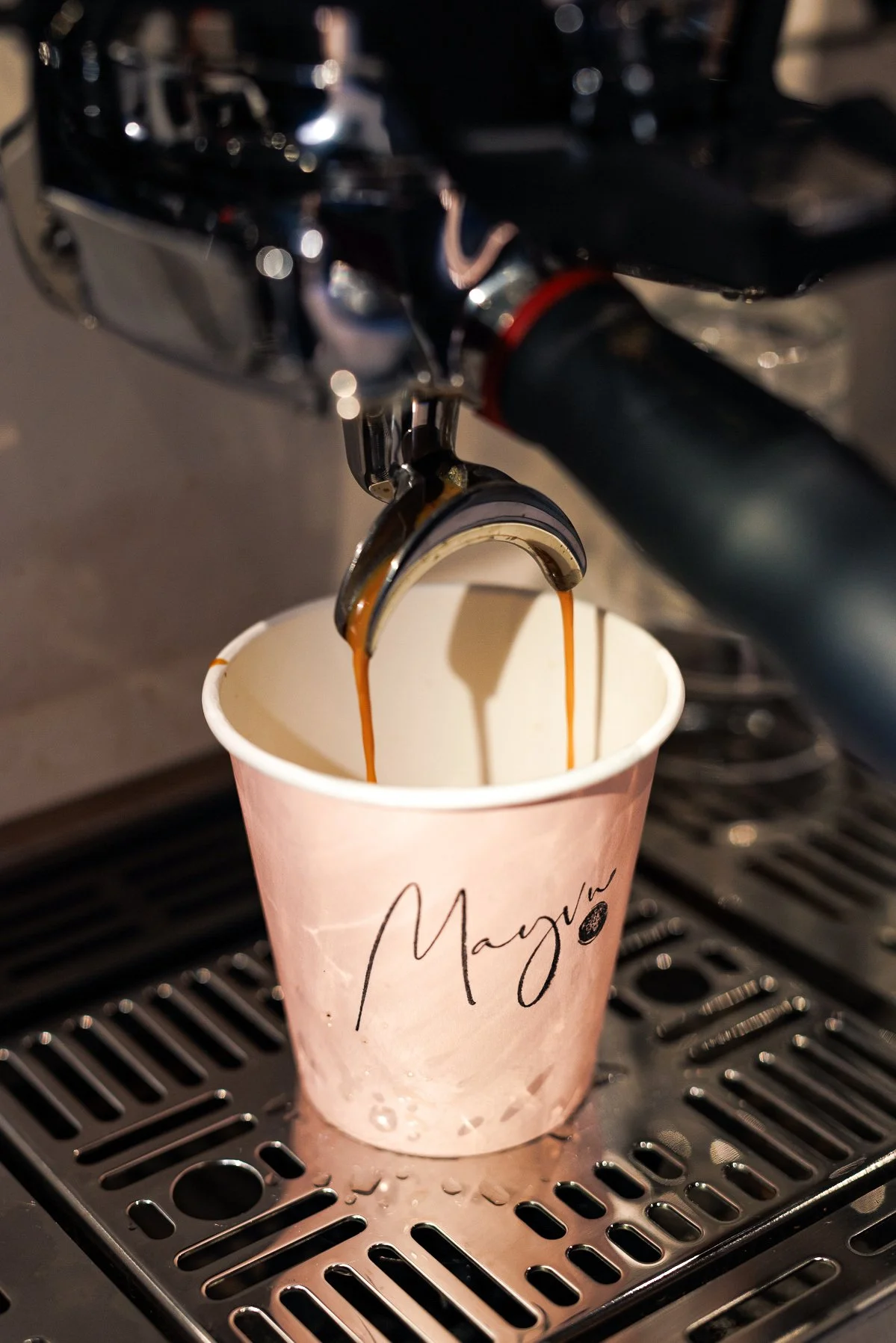 Coffee being poured from a coffee machine into a paper cup labeled 'Maya'.