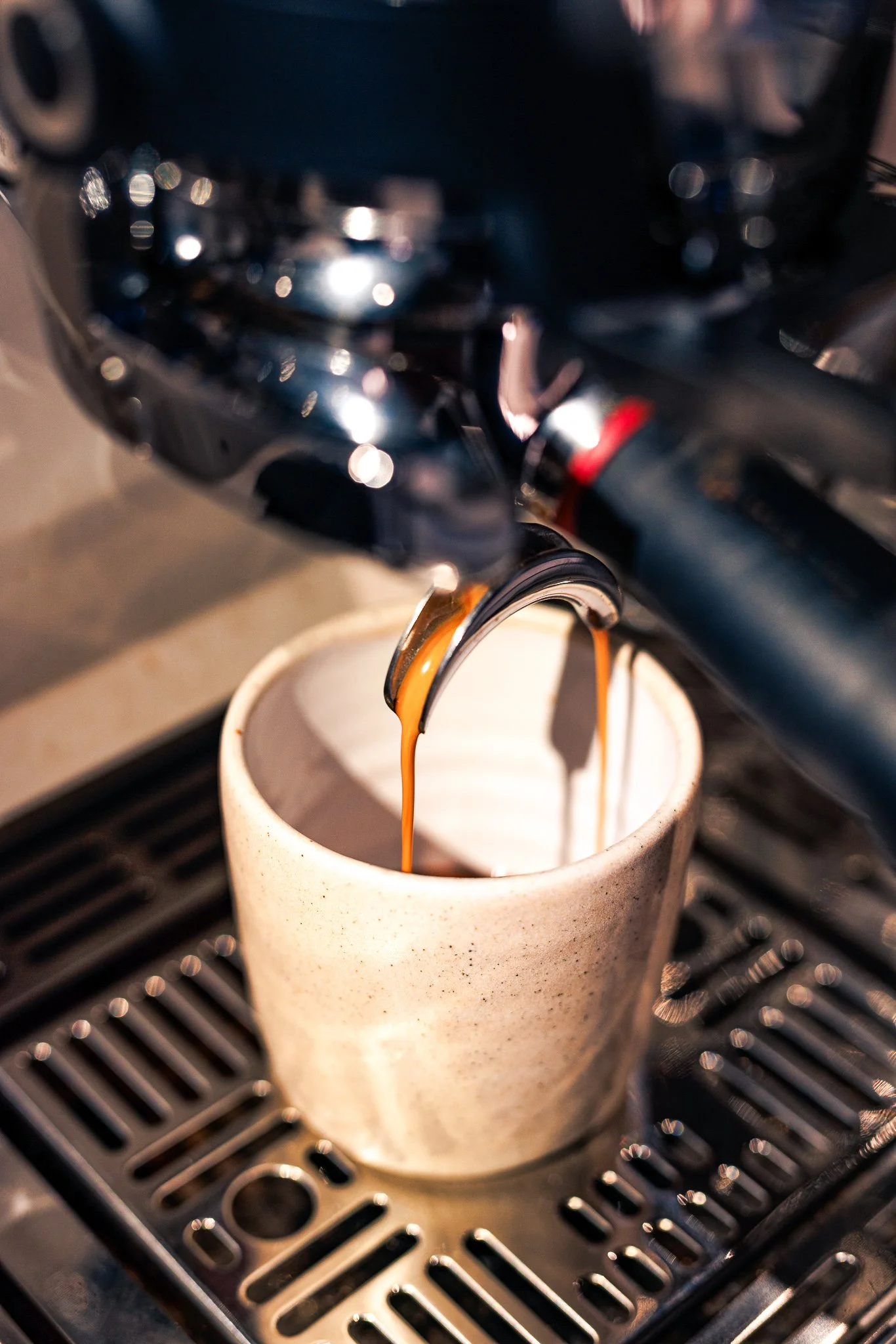Espresso being brewed into a mug from an espresso machine with a metallic spout, above a black drip tray.
