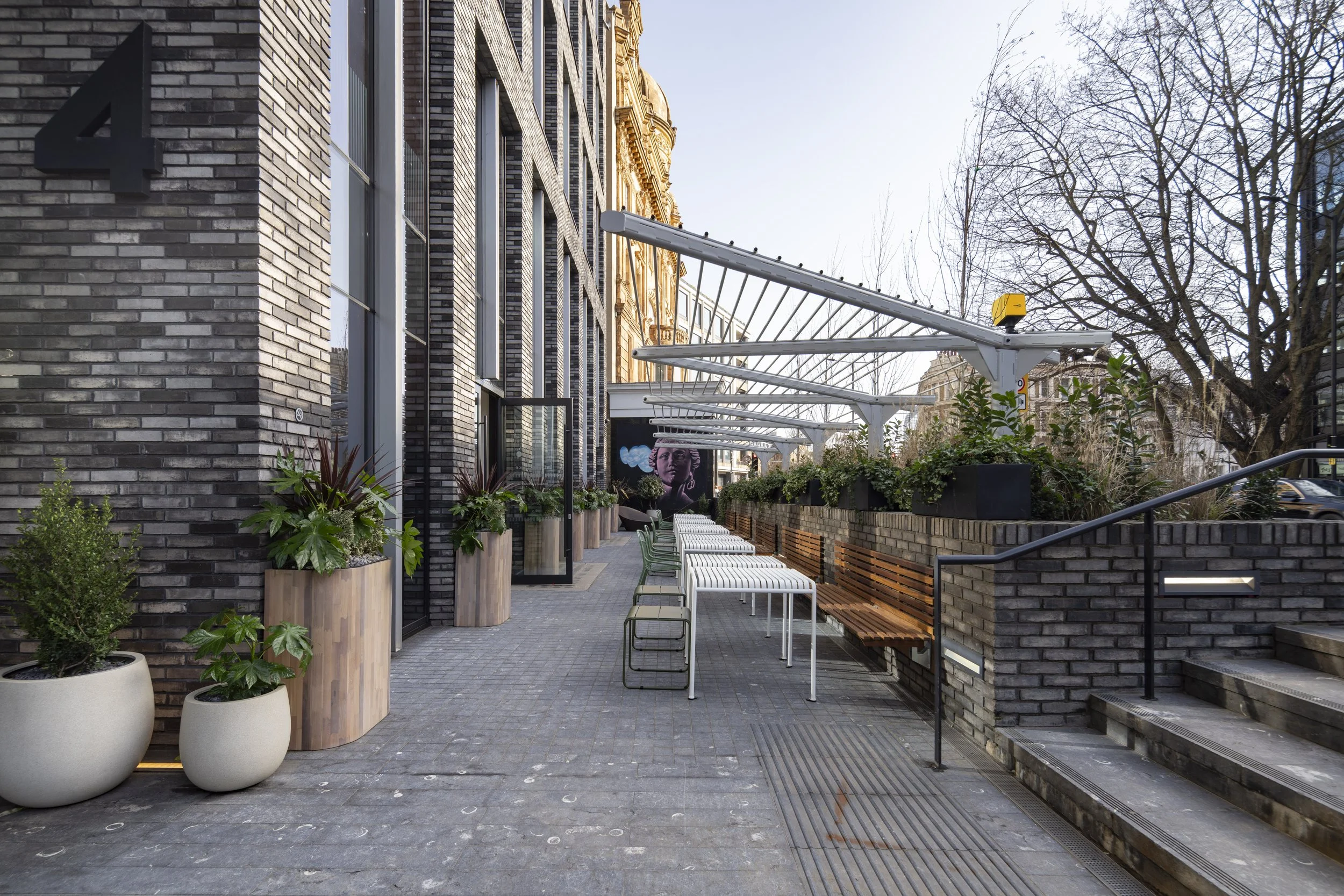 Empty outdoor seating area with potted plants, benches, and a mural in the background.
