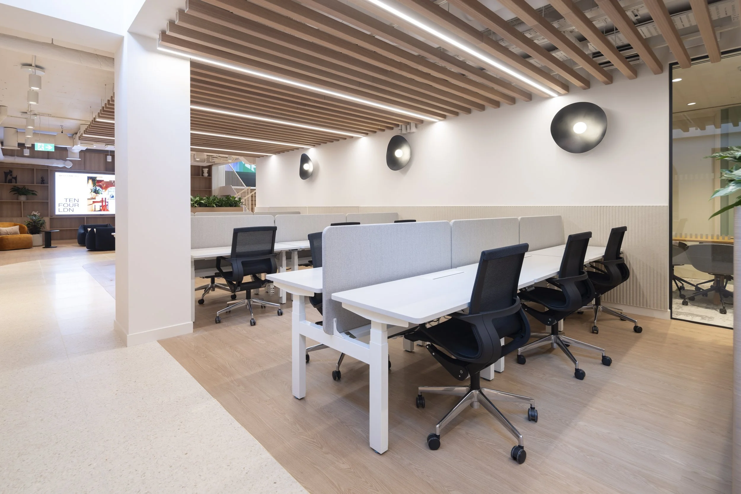 Modern office interior with white desks, black ergonomic chairs, decorative wall lights, wooden ceiling beams, and glass wall partitions.