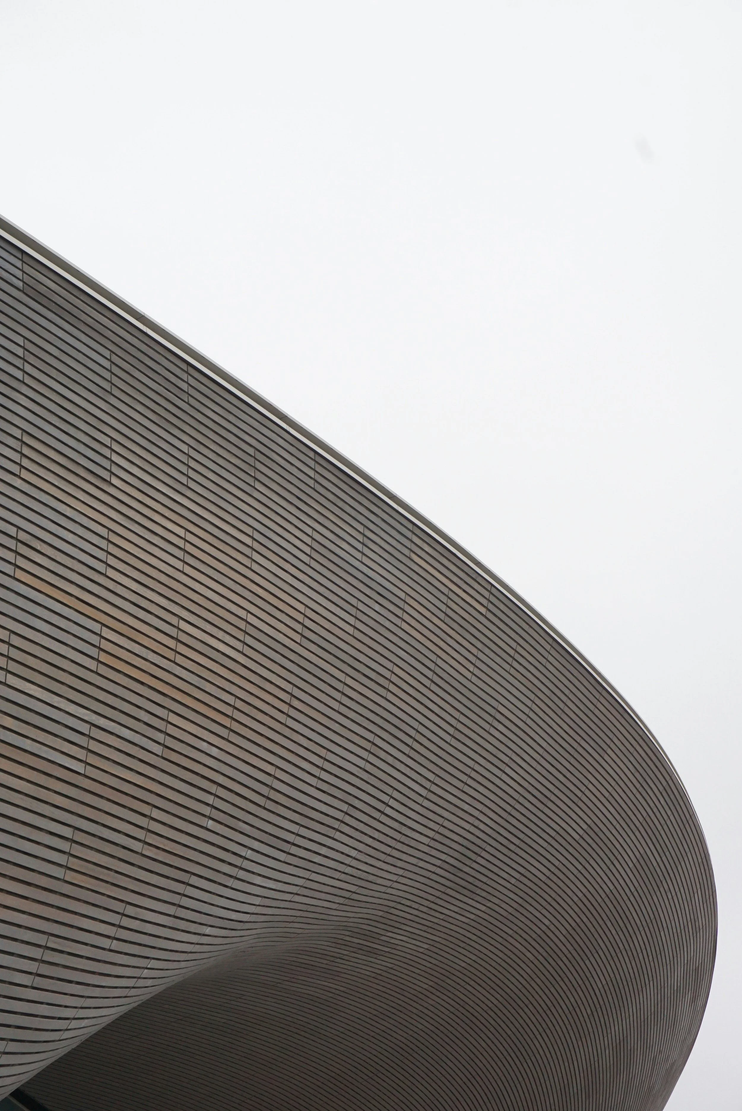 Close-up of a modern architectural building with curved, horizontal wooden slats on its facade, against an overcast sky.