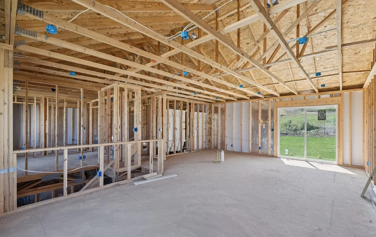 Interior of a house under construction with exposed wooden framing, a large window, and a concrete floor.