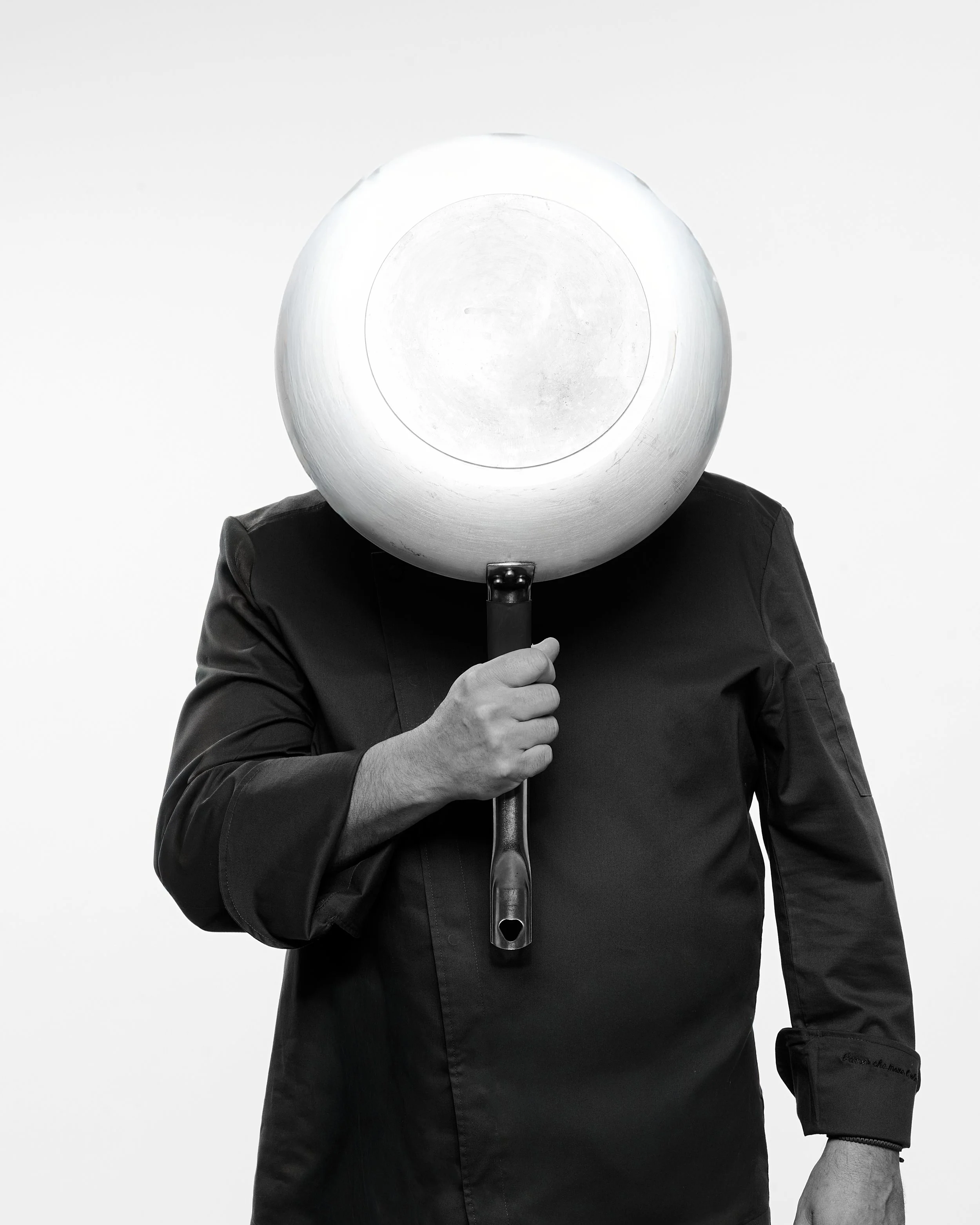 Persona con testa sostituita da un grande tagliere rotondo, coperto da una lampada, che tiene in mano un coltello