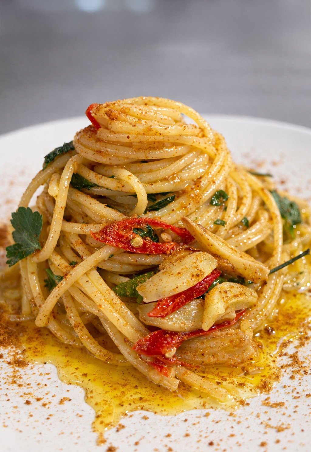 Piatto di spaghetti con aglio, peperoncino, prezzemolo e olio, disposto in modo artistico su un piatto bianco.