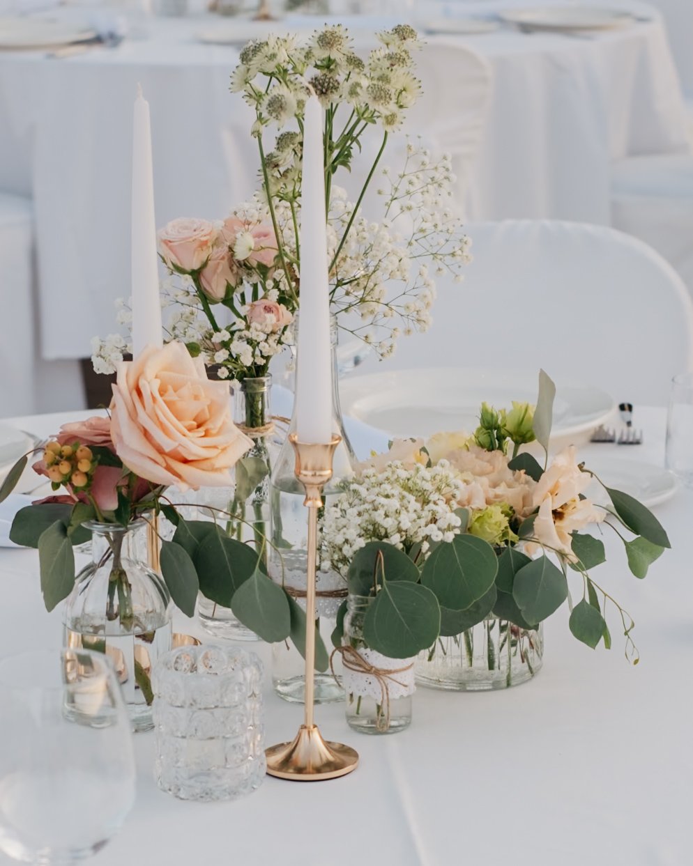 Elegant wedding table setting with white candles, floral arrangements, and glassware on a white tablecloth.