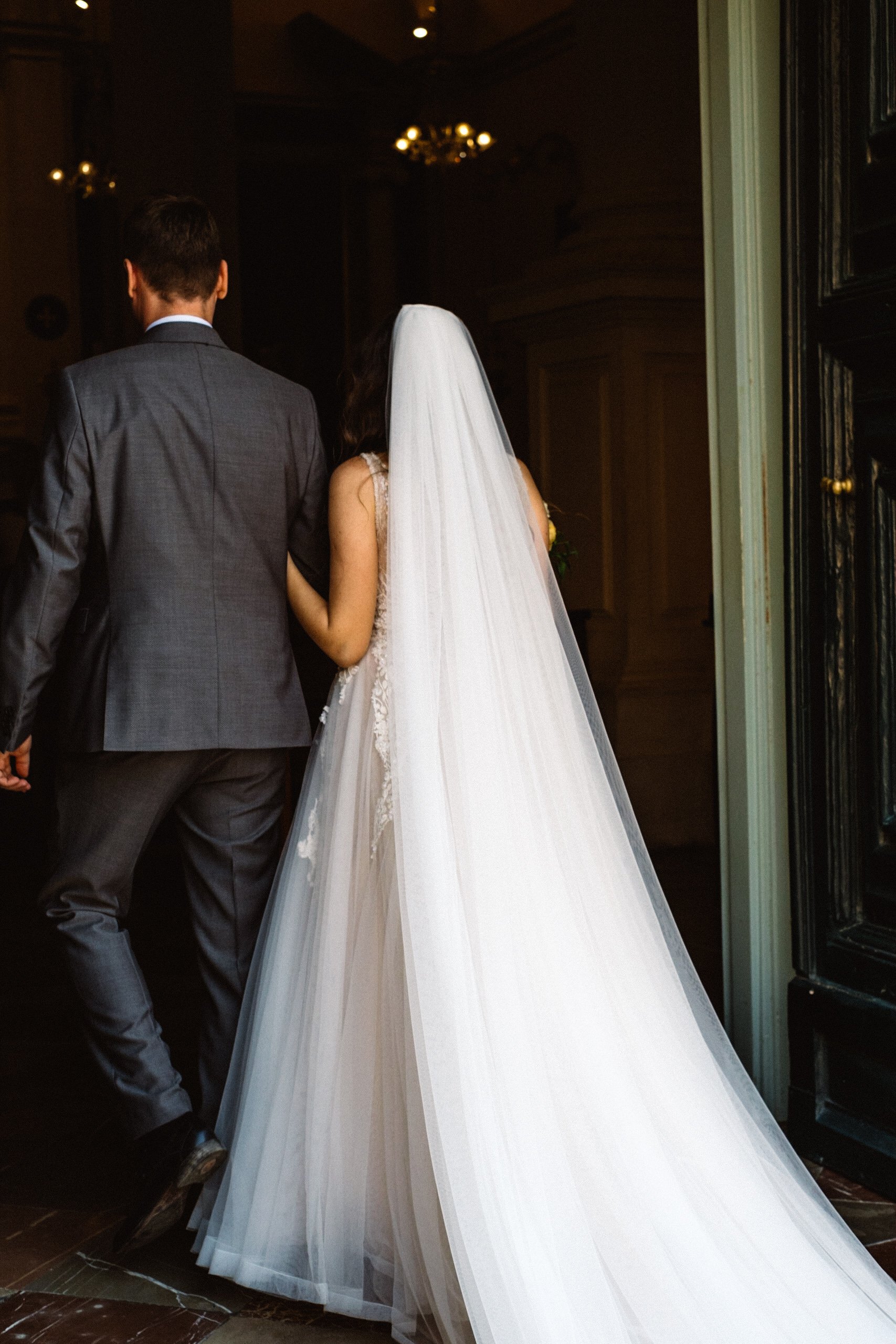 Bride and groom walking into a building, bride wearing a white wedding dress and veil, groom in a gray suit in Dubrovnik.