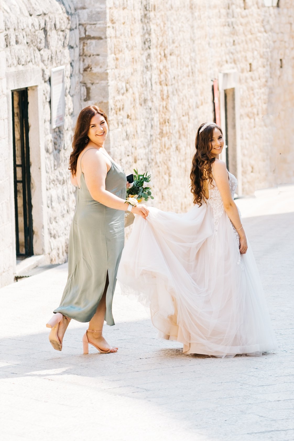 Bride walking with bridesmaid in historic alley of Dubrovnik Old Town.
