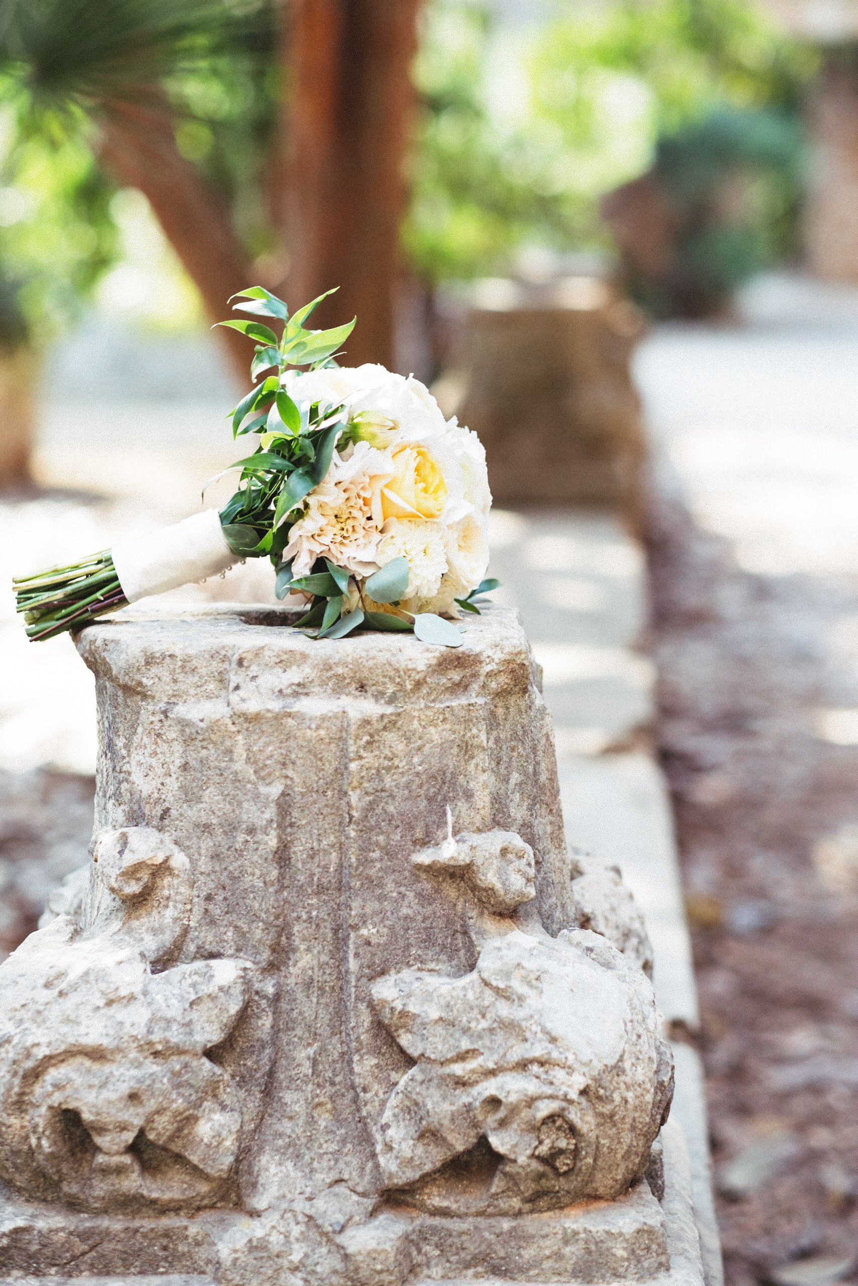 Bouquet of white and yellow flowers on stone pedestal outdoors.