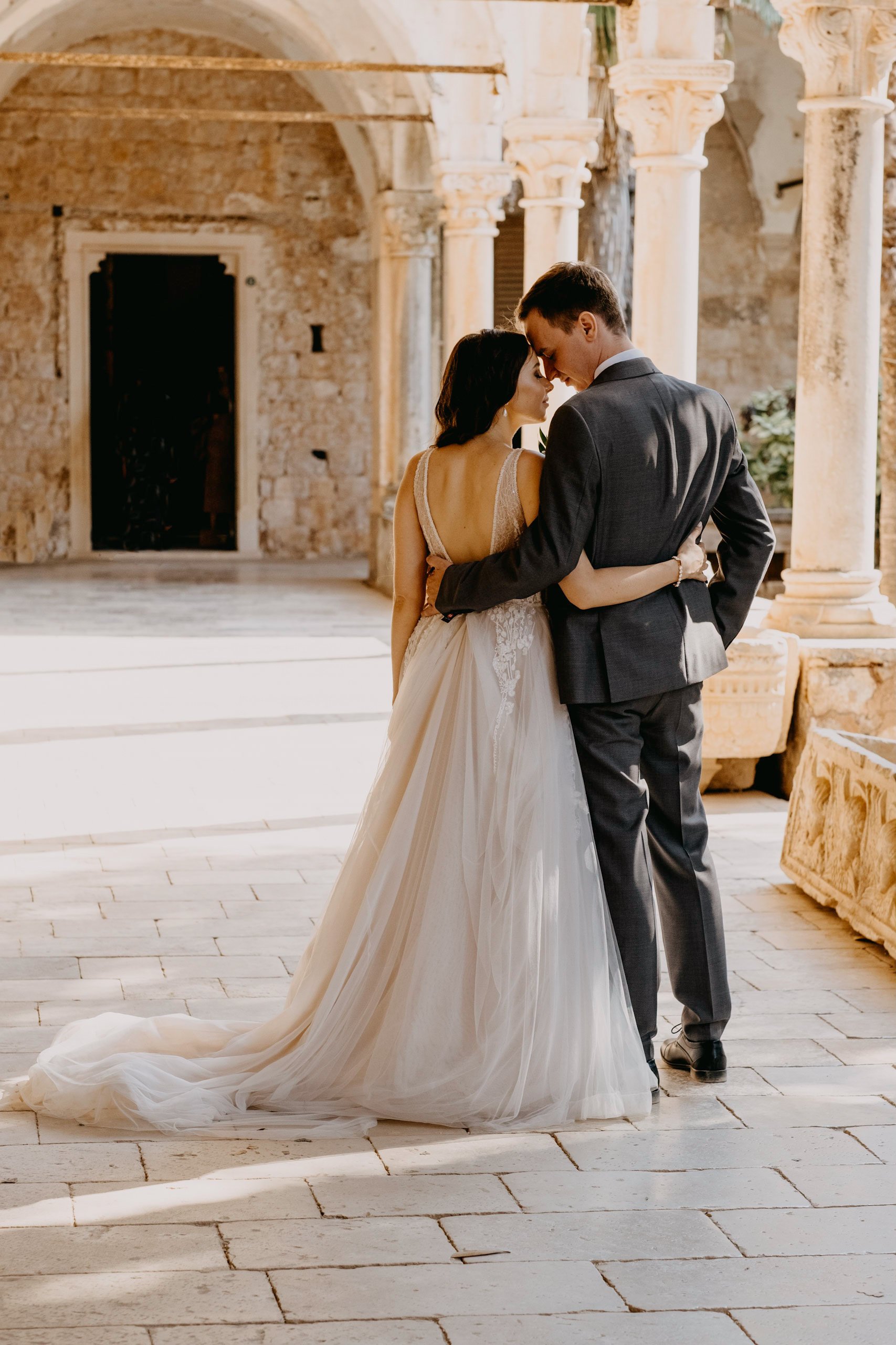 Bride and groom embracing under stone arches on Lokrum island in Dubrovnik, Croatia.