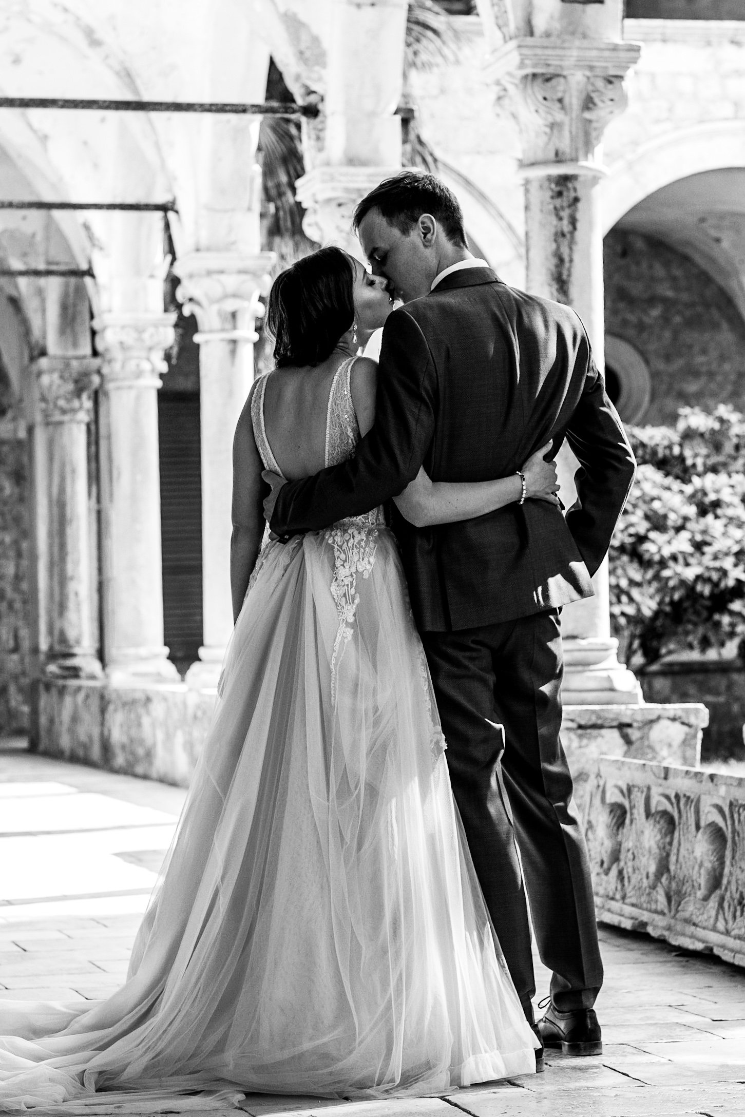 Black and white photo of a couple in formal attire, embracing in an ornate architectural setting.