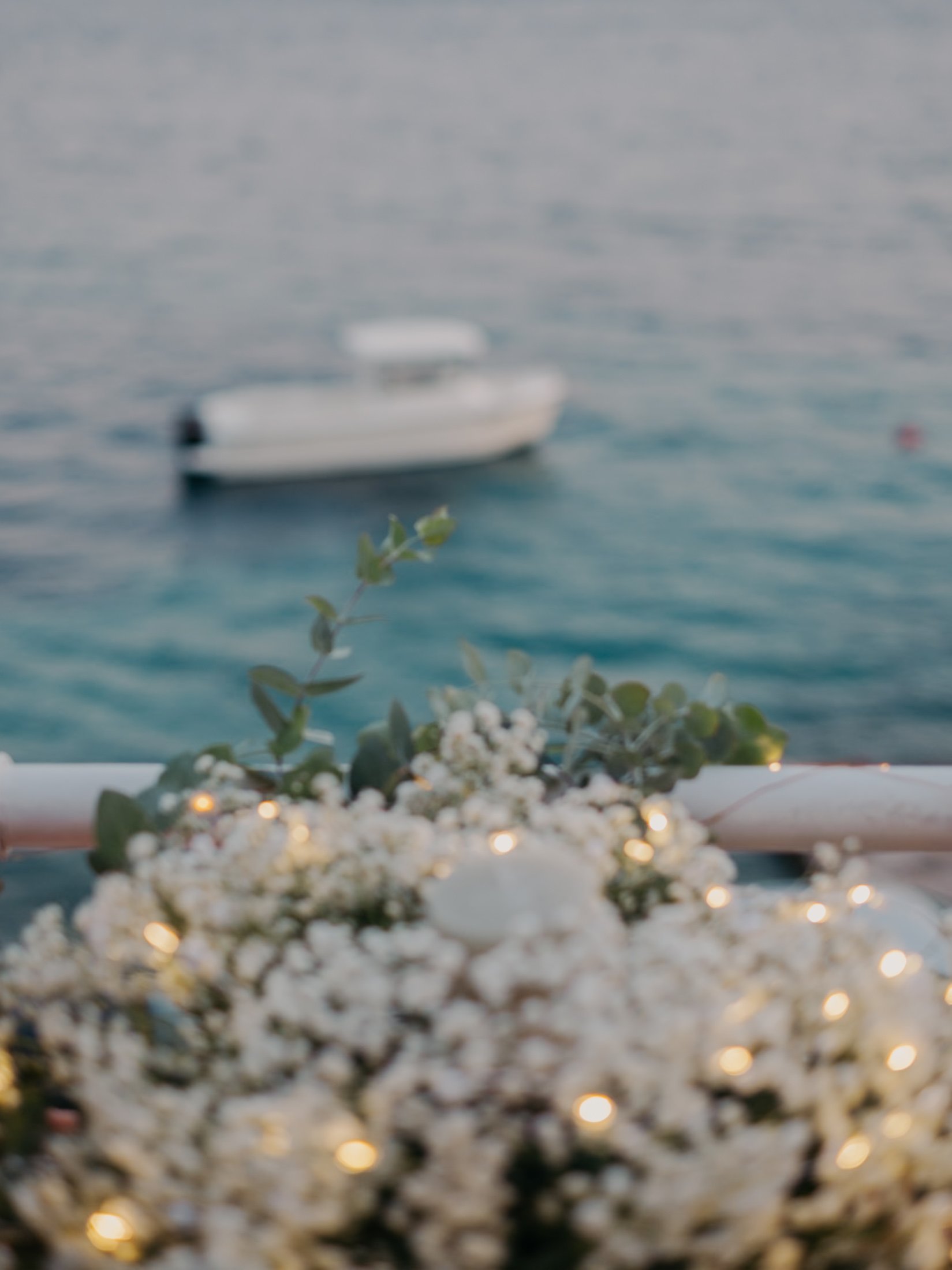 Out-of-focus boat on water with foreground of flowers and string lights.