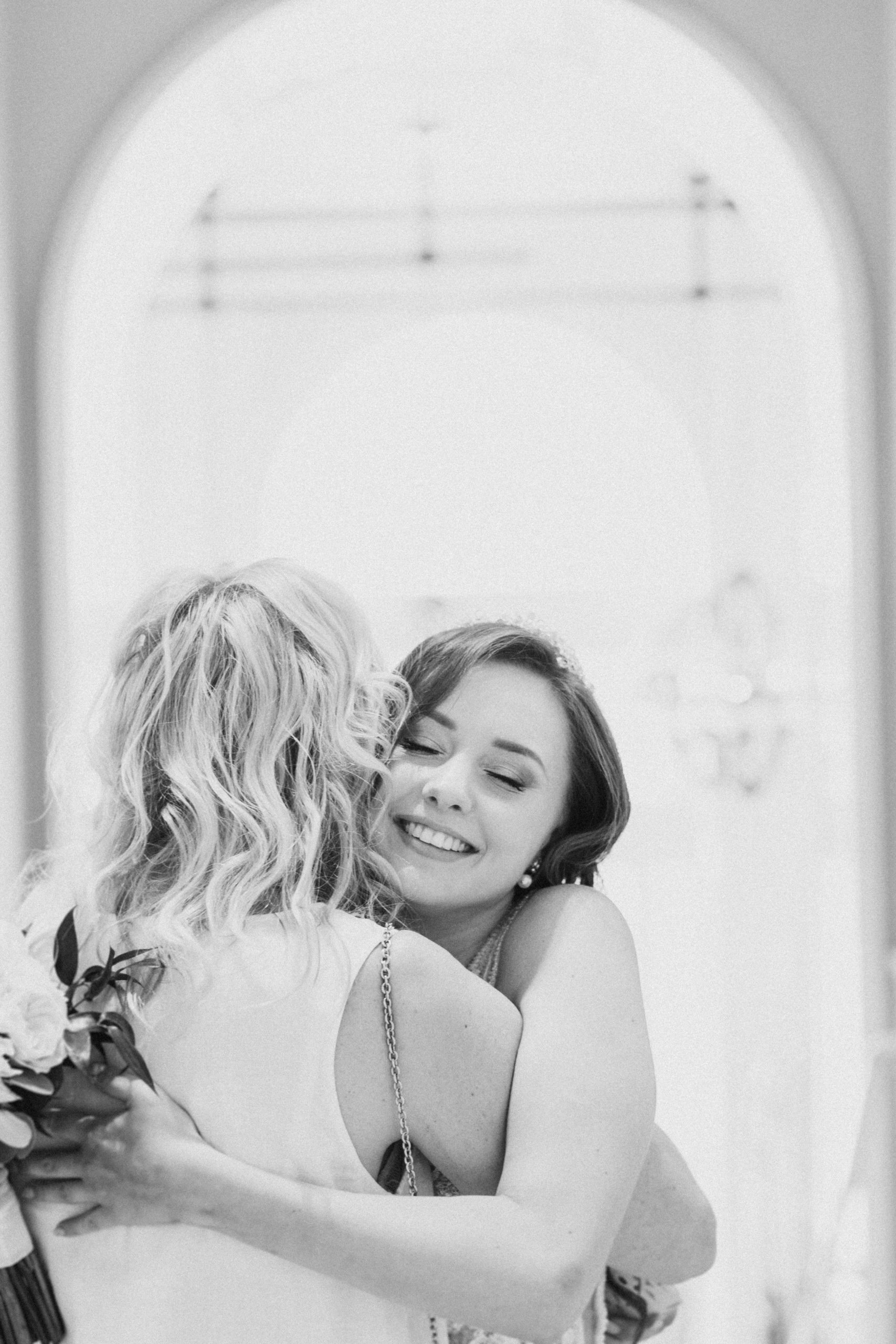 Two women hugging at a wedding, one holding a bouquet.