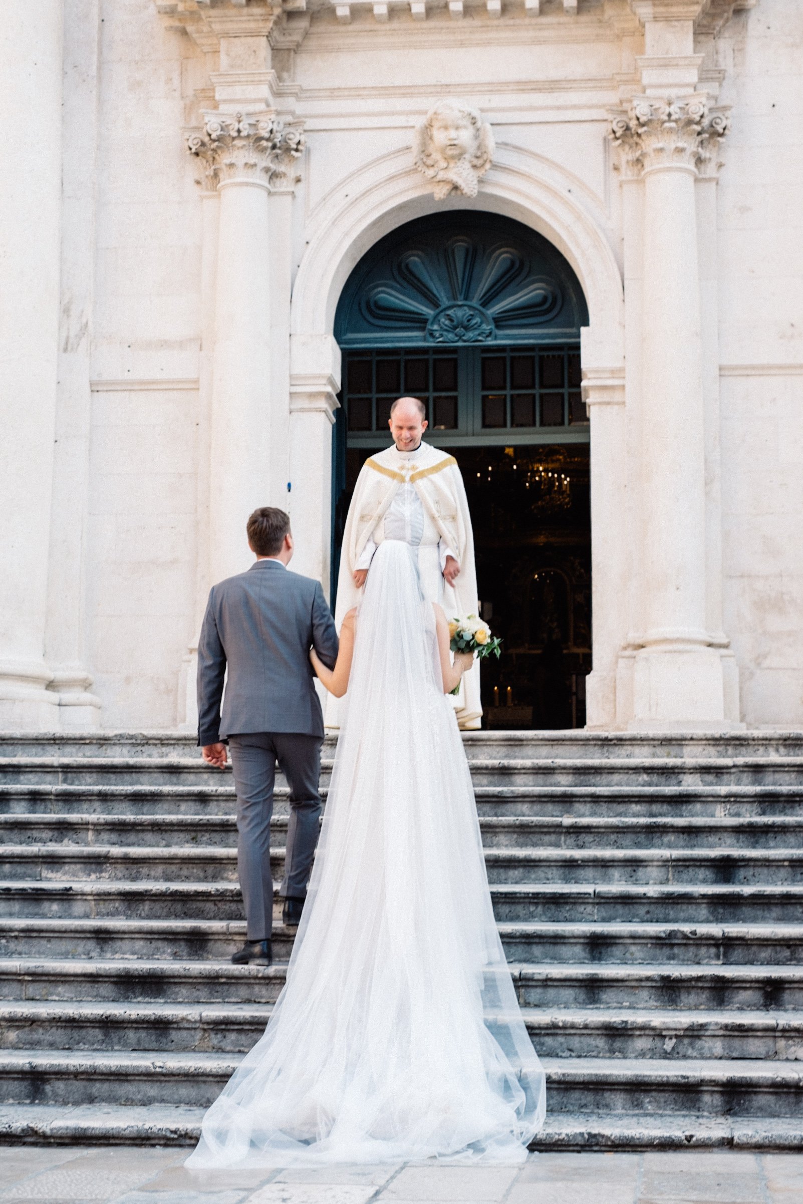 Bride and groom walking up church steps towards priest.