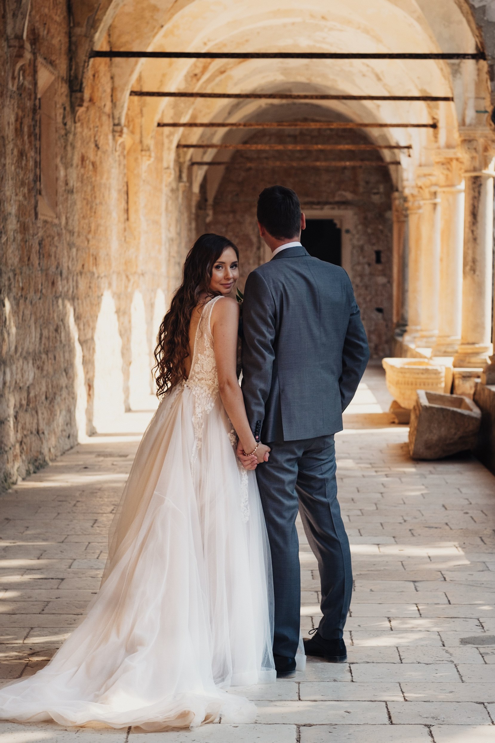Bride and groom holding hands in a historic stone corridor of monastery at Lokrum island in Dubrovnik.