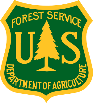 U.S. Forest Service emblem with a green shield, yellow border, and a yellow tree in the center, with text indicating Forest Service and Department of Agriculture.