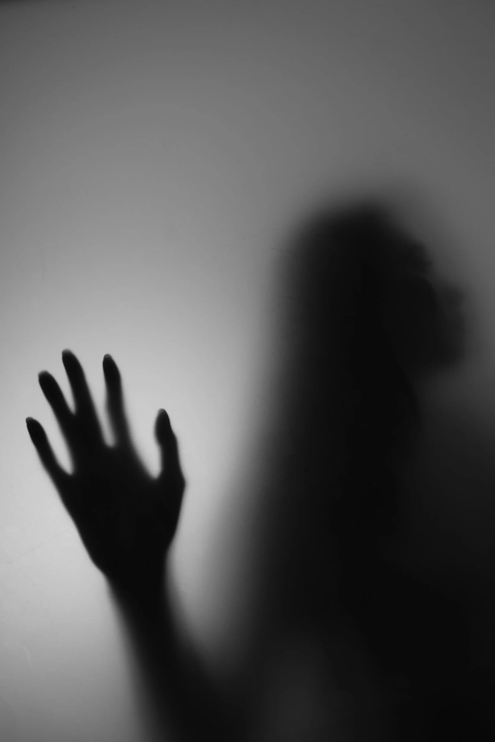 A blurry silhouette of a person with their hand pressed against a glass surface, creating a shadowed outline.