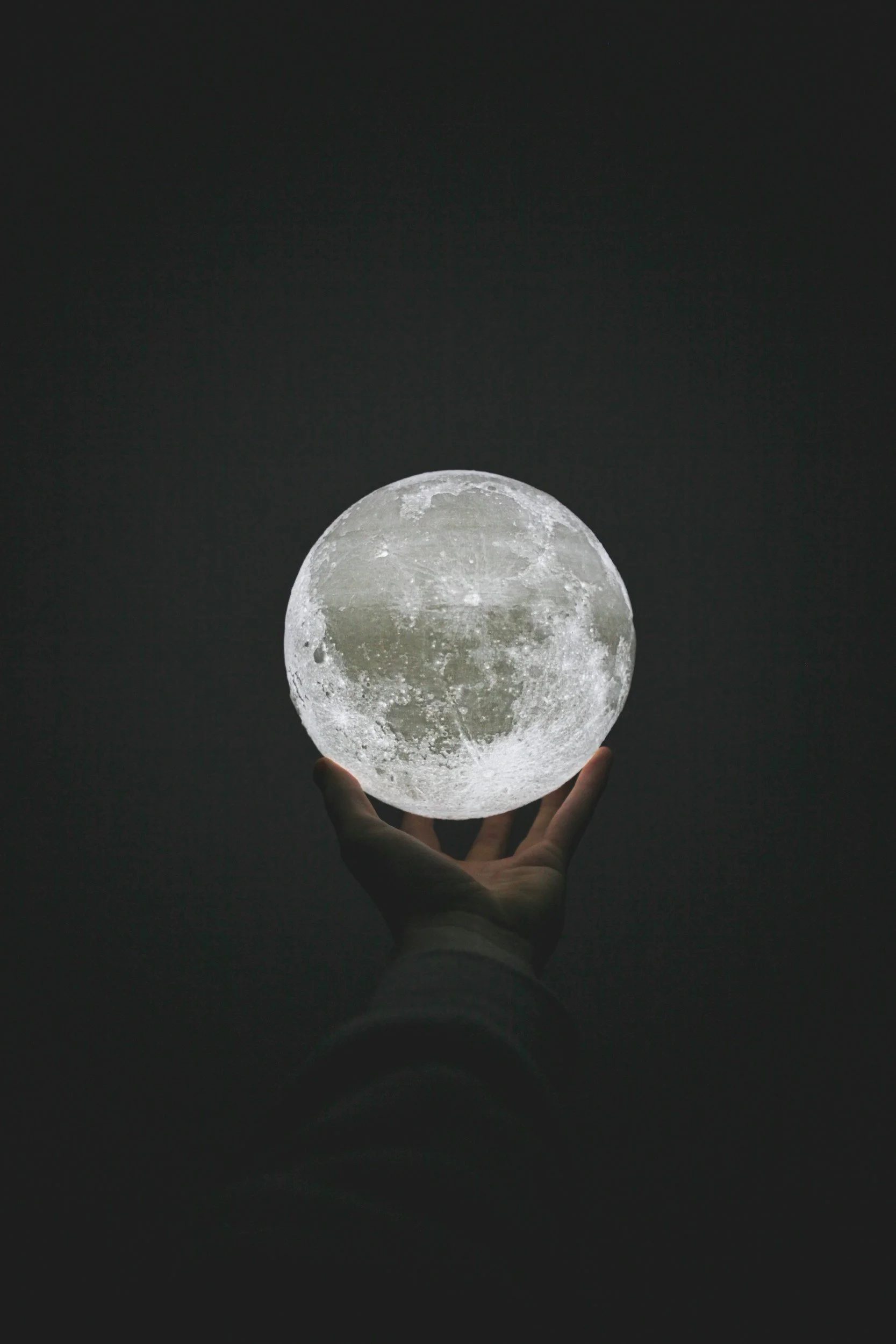 A hand holding a glowing moon-shaped object against a dark background.