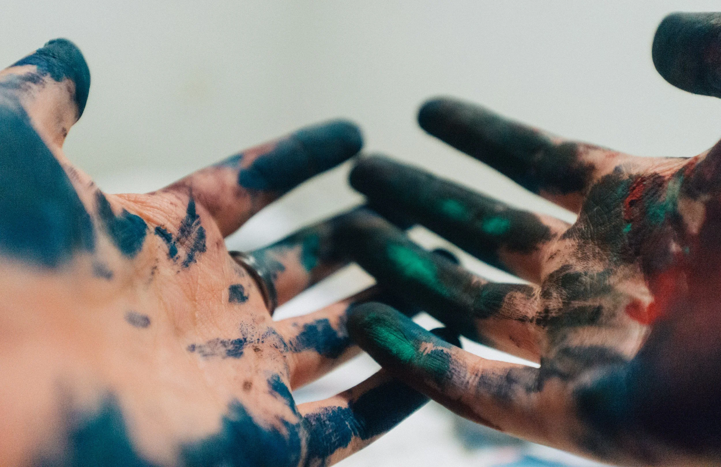 Close-up of two dirty hands with paint stains, reaching towards each other against a plain background.