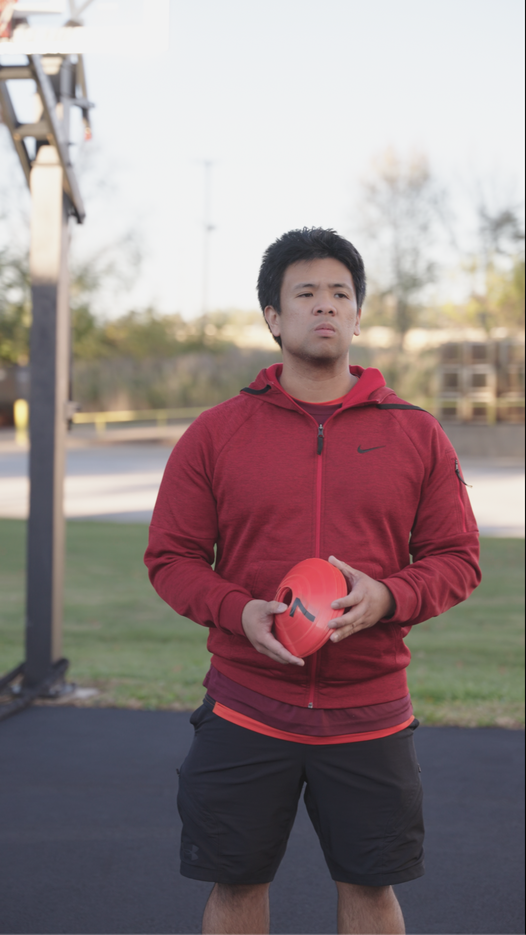A young man holding a red football standing outdoors on a sports field.