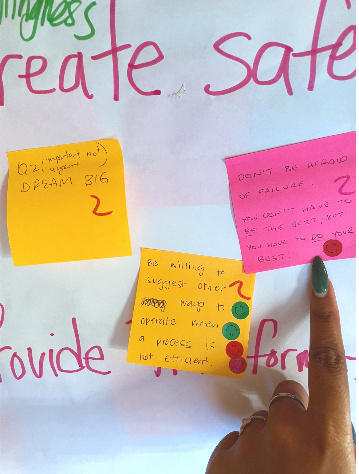Post-it notes with motivational quotes attached to a whiteboard or paper, and a person's hand with painted nails and rings pointing at the notes.