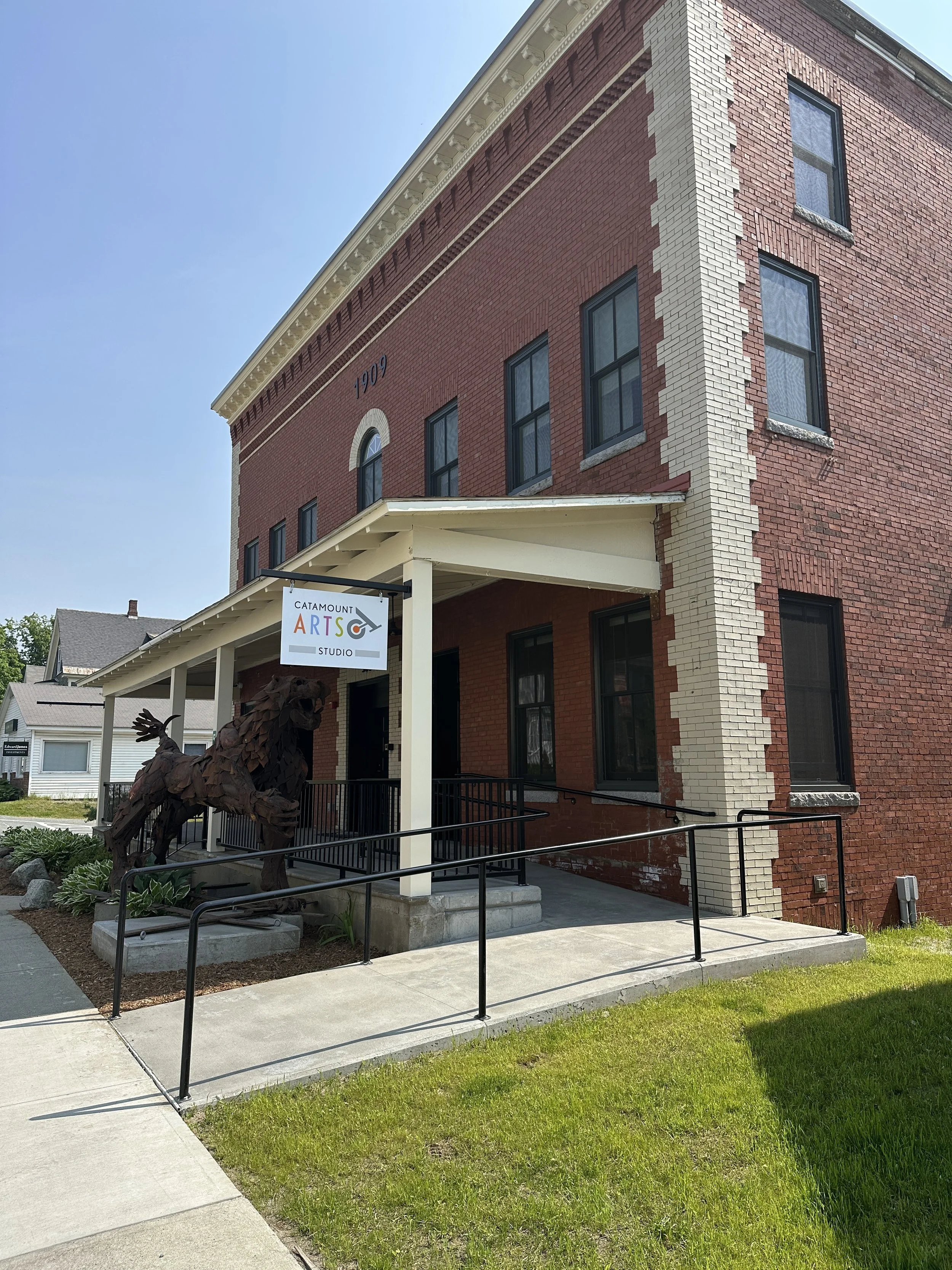 brick building with a sign that says, "Catamount Arts." Blue sky, horse sculpture in front of the building.